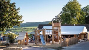 A playground with wooden structures, a slide, and a small building. - Huttopia Meursault (Meursault)