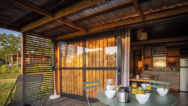 A covered outdoor dining area with a table set for breakfast, including bowls, a coffee pot, and a fruit basket. - Huttopia Meursault (Meursault)