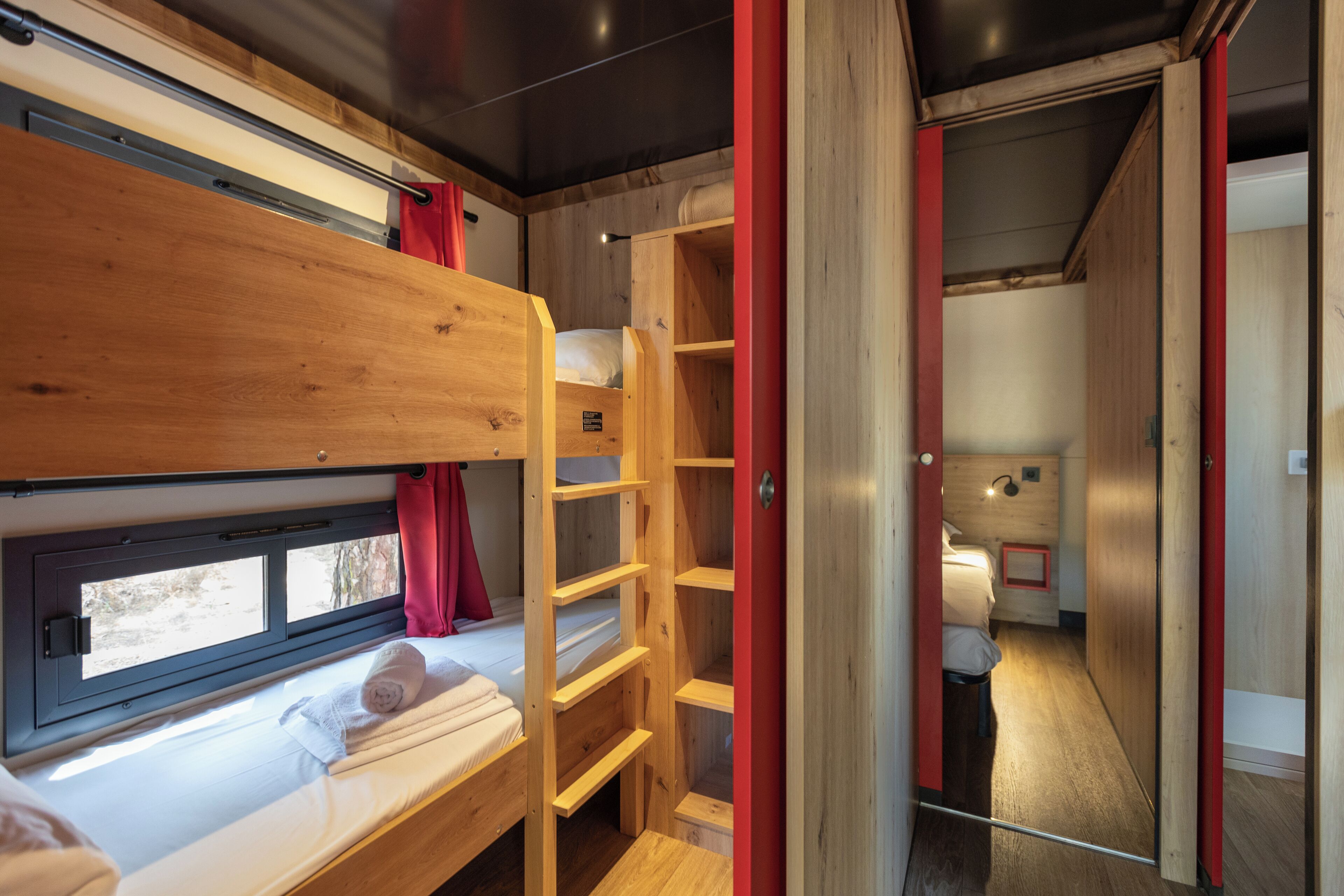 A compact train compartment with bunk beds, a wooden ladder, and a small window.