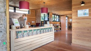 A wooden reception desk with a red hanging lamp, a glass display case, and a menu board. - Huttopia Meursault (Meursault)