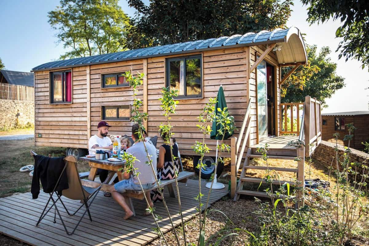 Une cabane en bois dotée d’une terrasse, d’un porche couvert et d’un petit espace extérieur aménagé pour s’asseoir.