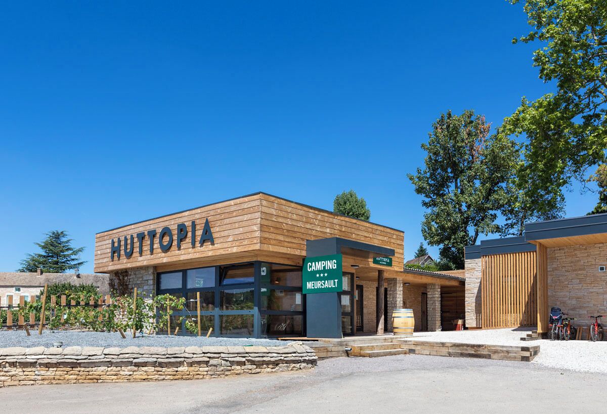 Un bâtiment moderne avec une enseigne indiquant « HUTTOPIA » et une autre précisant « CAMPING MEURSAULT ».