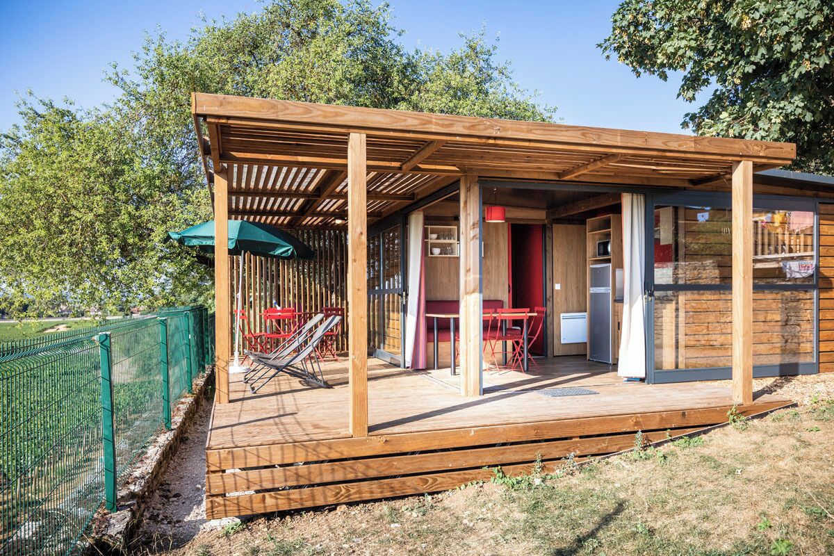Terraza de madera con un porche cubierto, mobiliario exterior y un jardín cercado.
