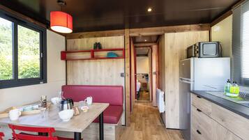 A compact kitchen with wooden cabinets, a dining table with red chairs, a small refrigerator, and a television on top.