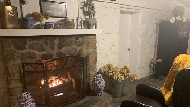 Een gezellige woonkamer met een stenen openhaard, een zwarte leren fauteuil en decoratieve objecten op de schoorsteenmantel.