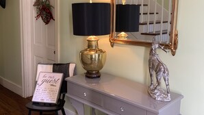 Een gang met een console tafel, een spiegel, een lamp, een kleine stoel en een welkomstbord.