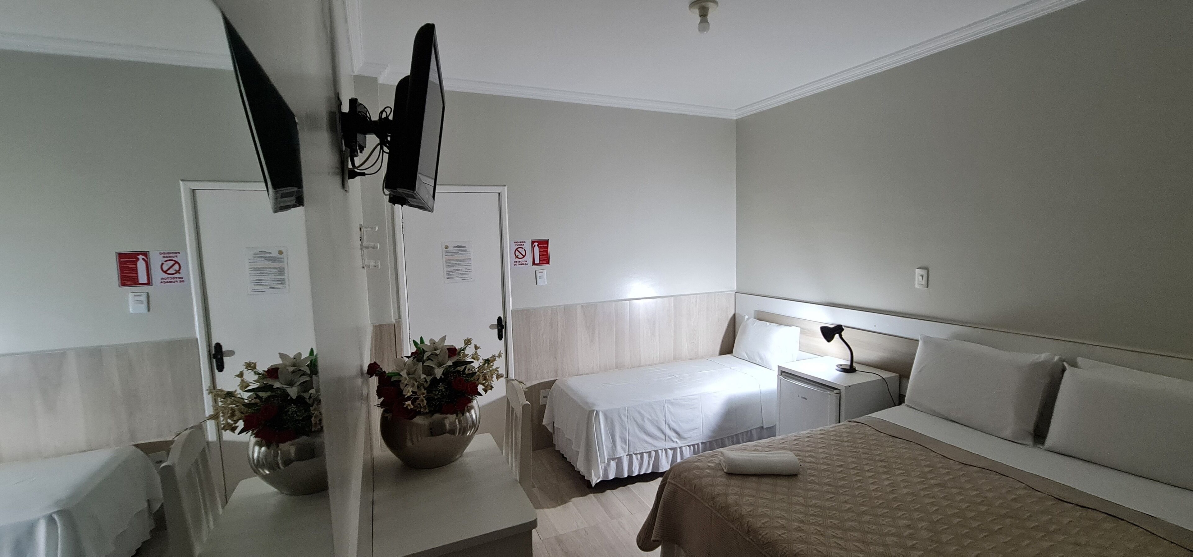 Hotelkamer met twee eenpersoonsbedden, een nachtkastje met een lamp, een spiegel, een bloevas en een deur met een spiegel en een bordje.