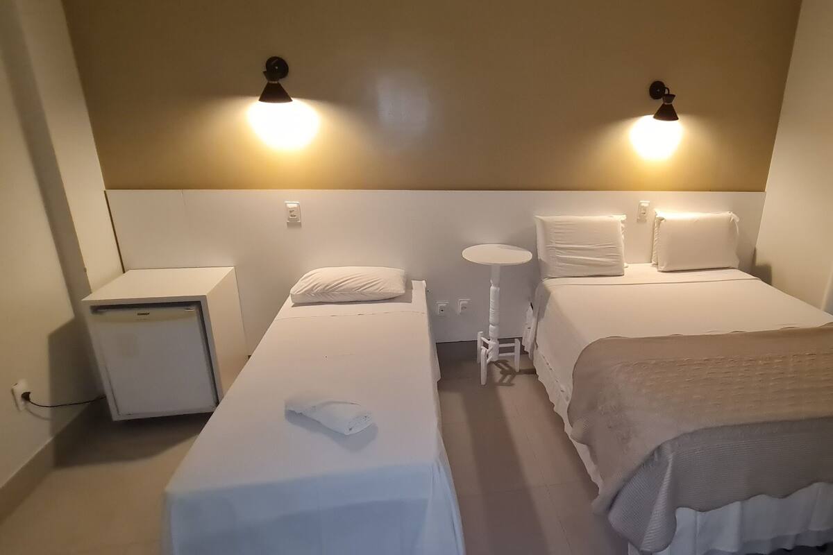 A hotel room with two single beds, a small round table, and a nightstand with a lamp.
