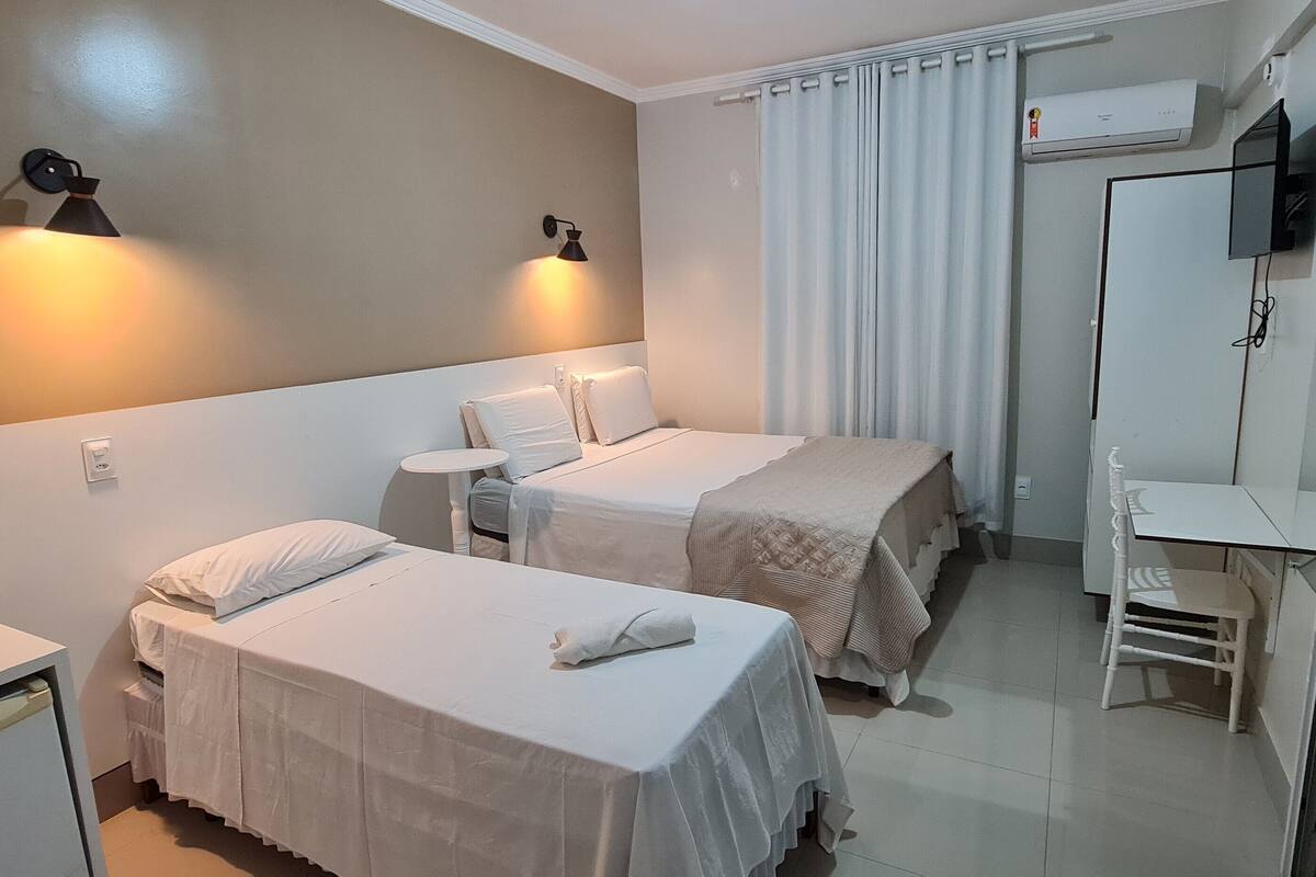 A hotel room with two single beds, a small desk, a chair, and a television mounted on the wall.