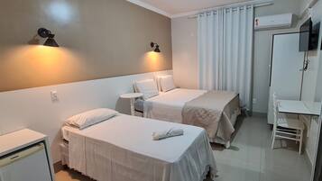 Quarto de hotel com duas camas de solteiro, uma pequena mesa de trabalho, uma cadeira e uma televisão fixada na parede.