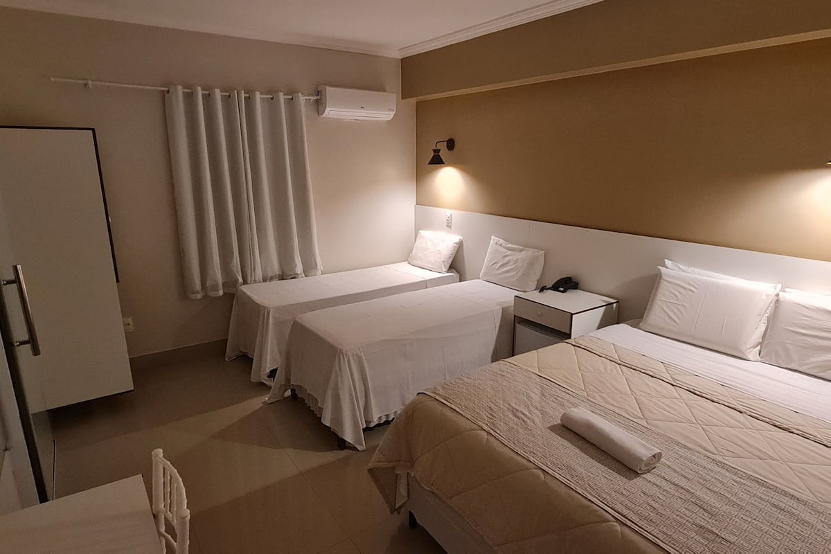 A hotel room with two single beds, a large bed, a desk, a chair, a TV, and a curtain.
