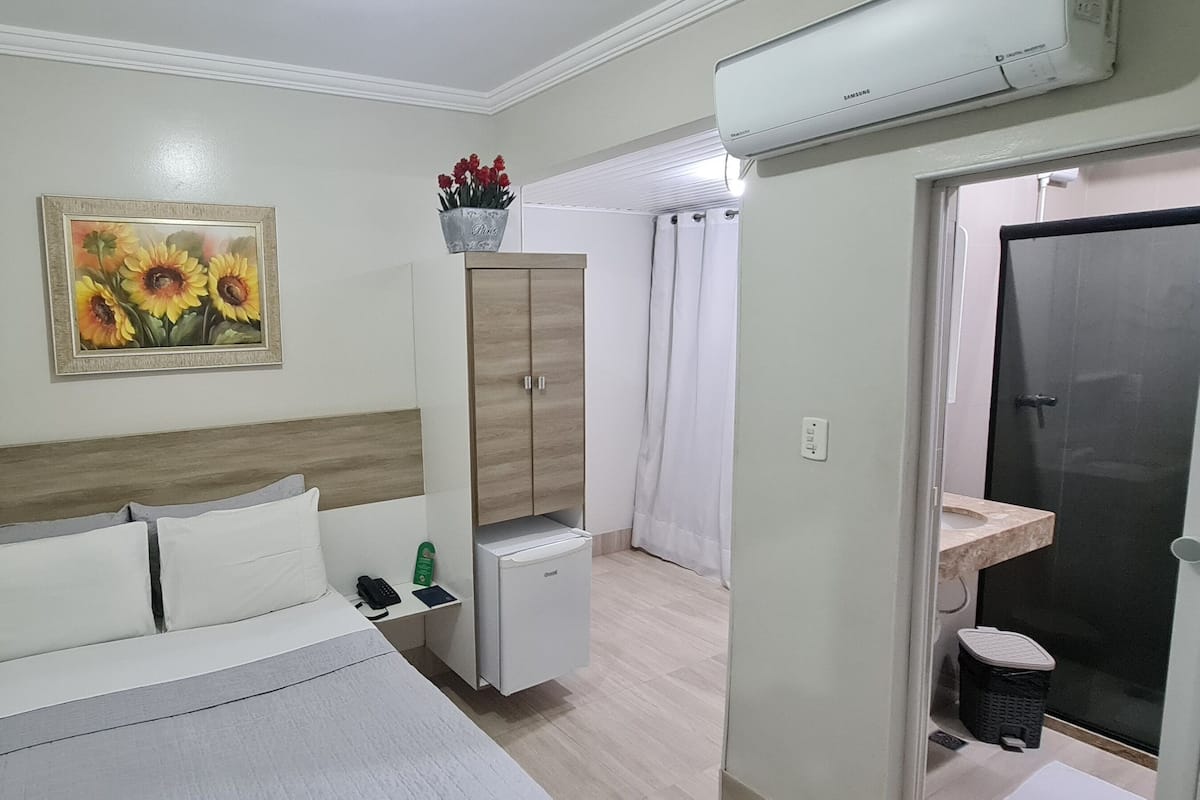 A hotel room with a bed, a small cabinet, a sink, and a shower area.