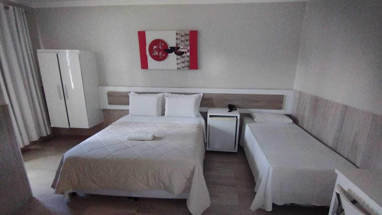 A hotel room with a large bed, a smaller bed, a nightstand, a refrigerator, and a wall art piece.