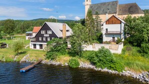 A riverside town with a church, a wooden house labeled 'JEZERKA', and a dock with a boat. - Lipno Lake Chalet (Prední Výton)