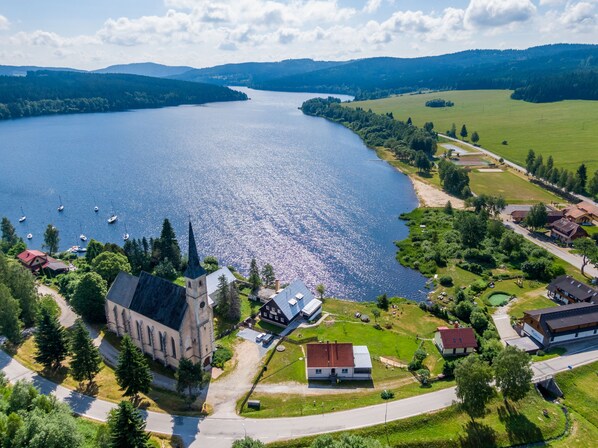 An aerial view of a lakeside village with a church, residential houses, and boats on the lake. - Lipno Lake Chalet (Prední Výton)