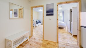 A hallway with wooden flooring, a white bench, and a bed in the background. - Lipno Lake Chalet (Prední Výton)
