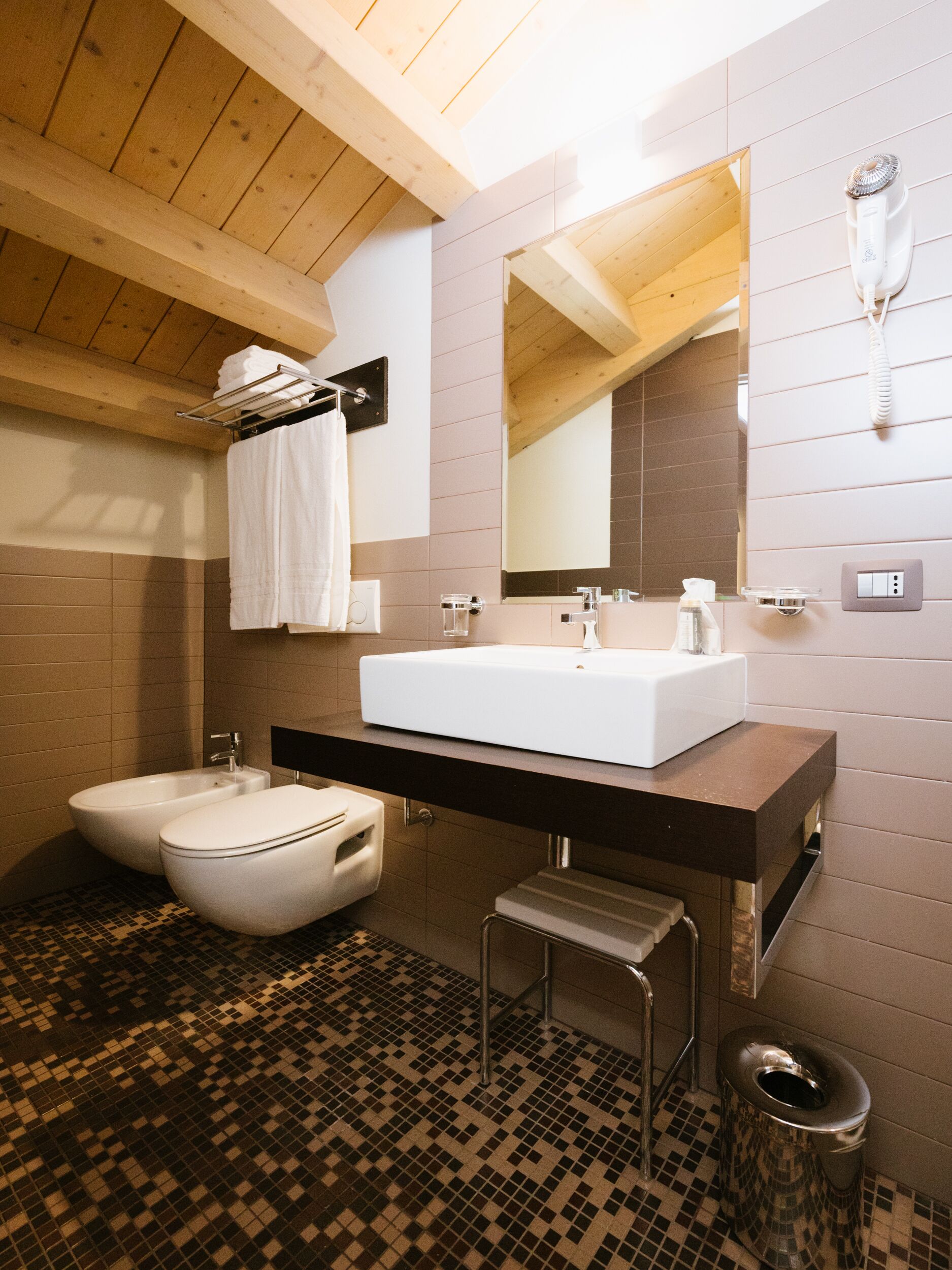 Un baño moderno con techo de madera, un lavabo blanco, un bidé y piso de baldosas.