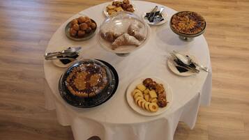 Una mesa redonda con diversos postres y pasteles, incluyendo un pastel de frutas, hojaldras y un bizcocho, sobre un mantel blanco.