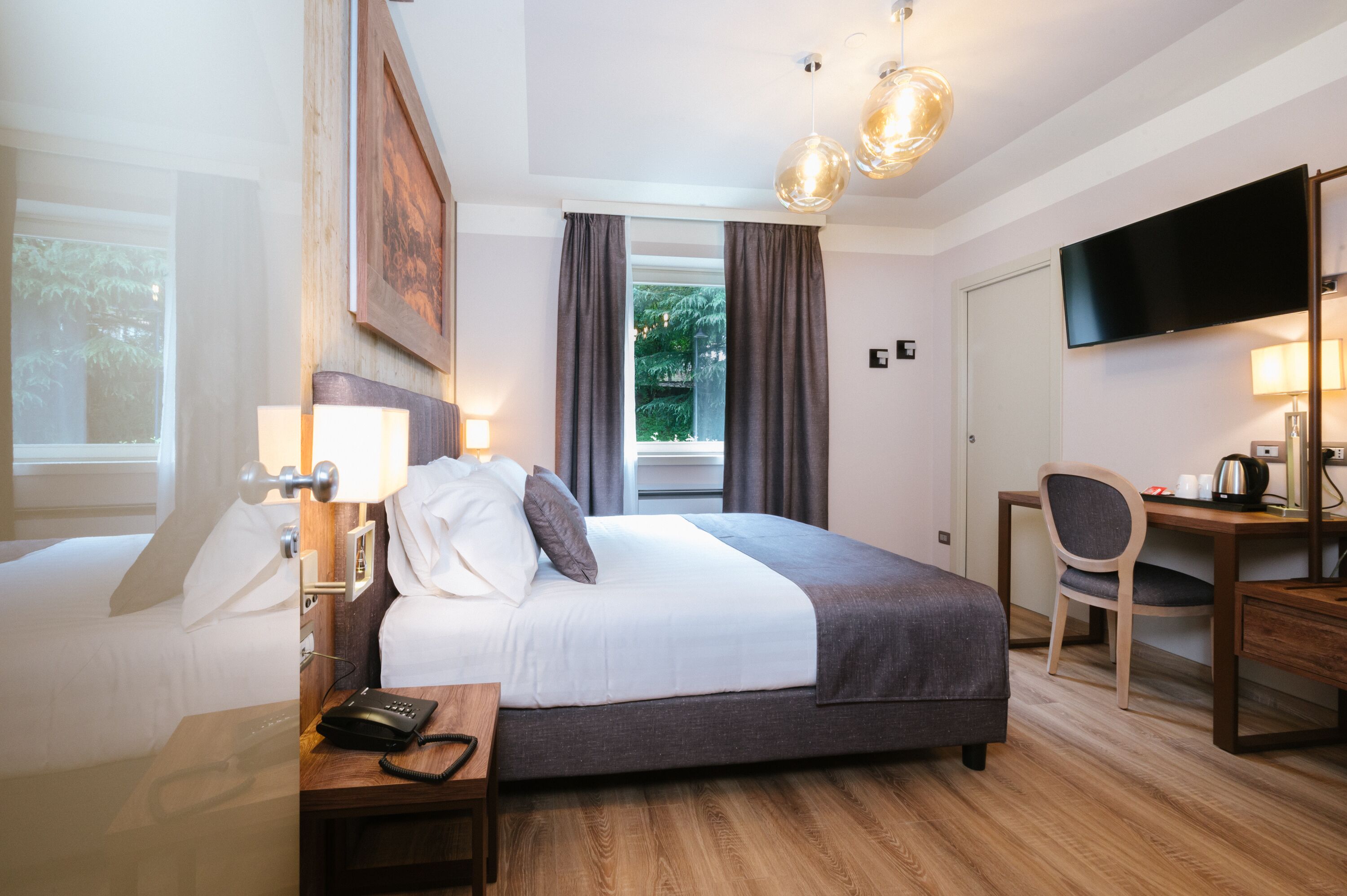 Ein Hotelzimmer mit Bett, Nachttisch, Lampe, Schreibtisch, Stuhl und Fernseher.
