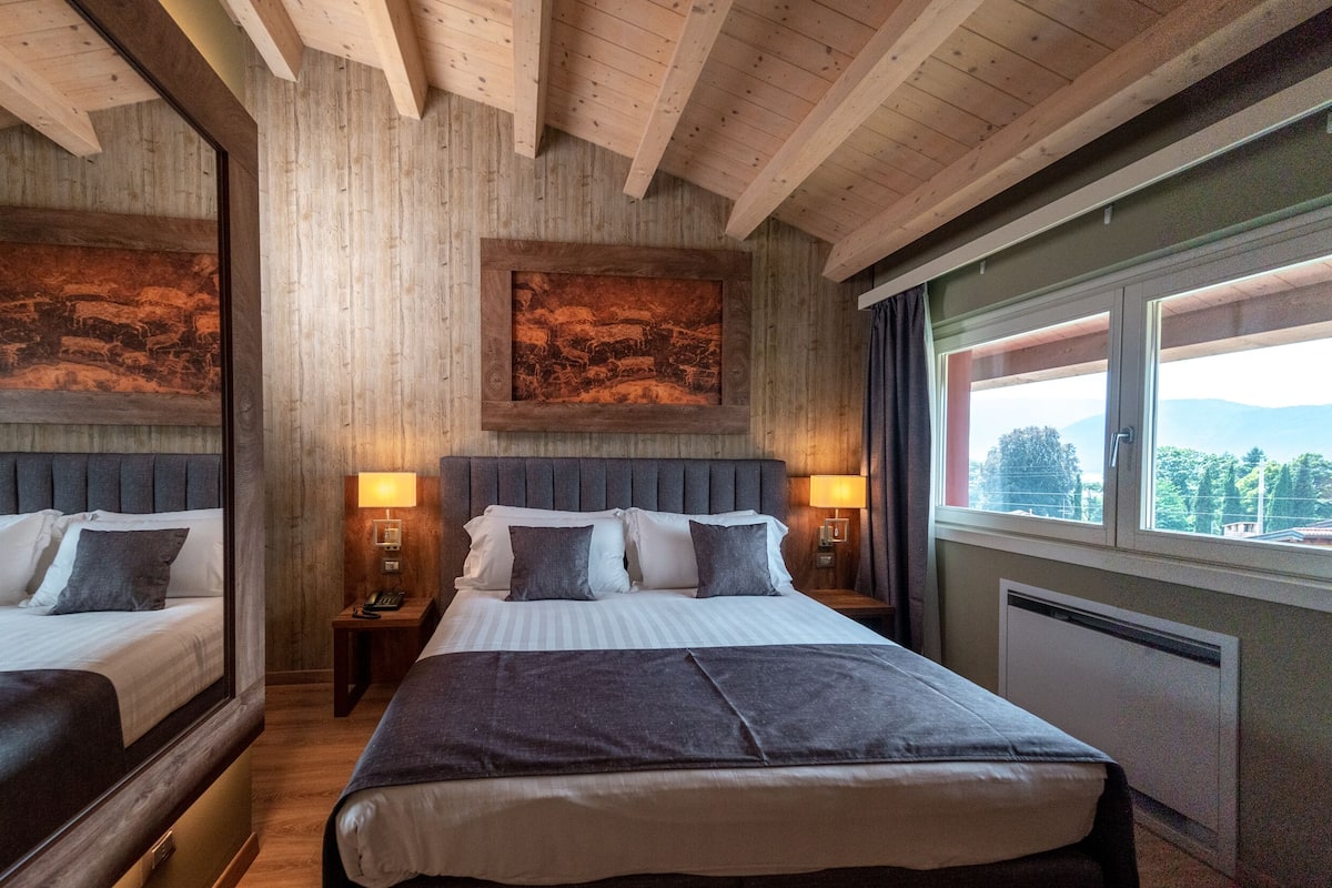 A double bed with a headboard, two bedside tables, a nightstand, a framed picture, and a window with a view.
