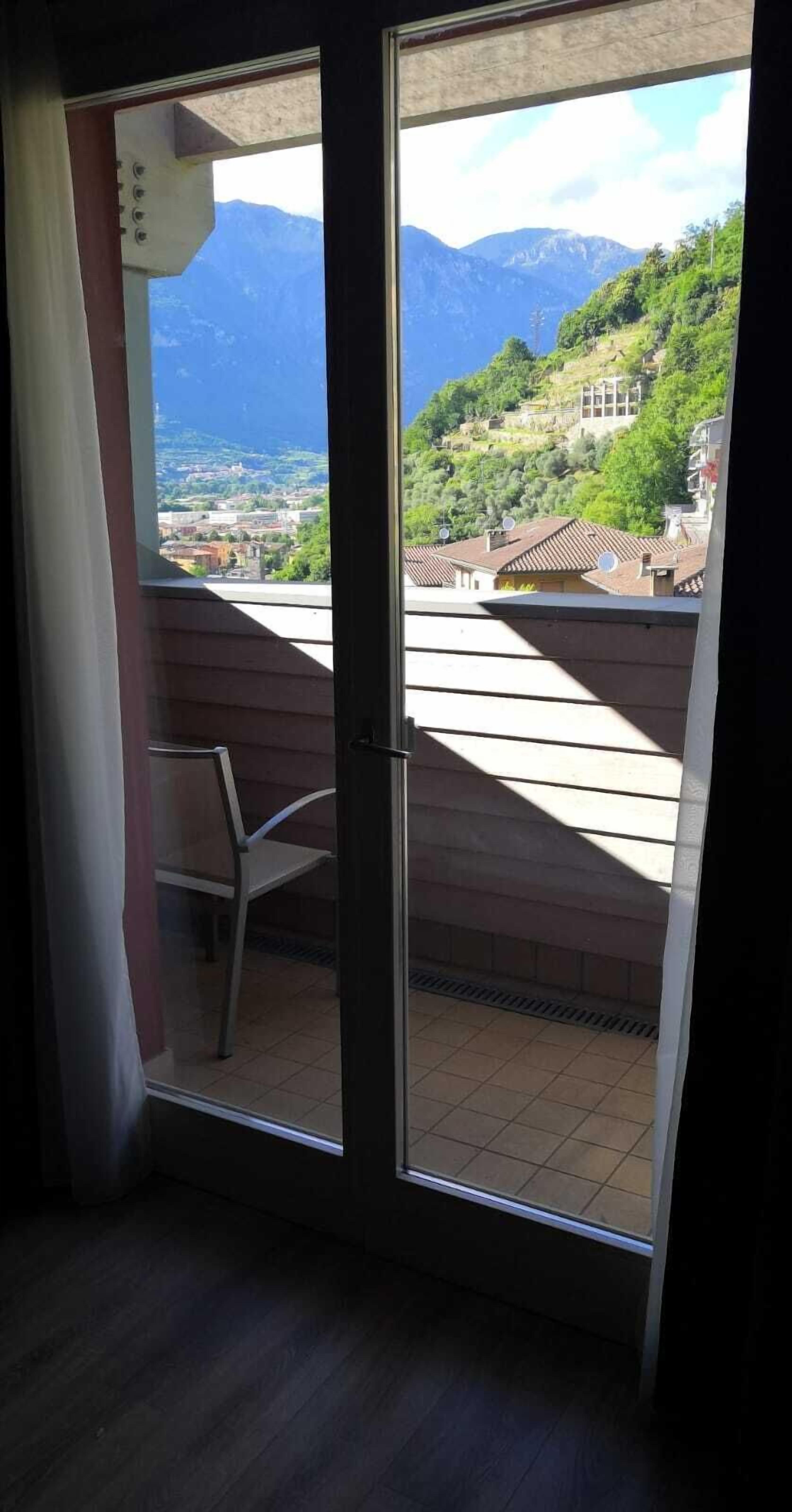 Una habitación con puerta de vidrio corrediza que da a un balcón con vistas a un paisaje montañoso y un pueblo abajo.