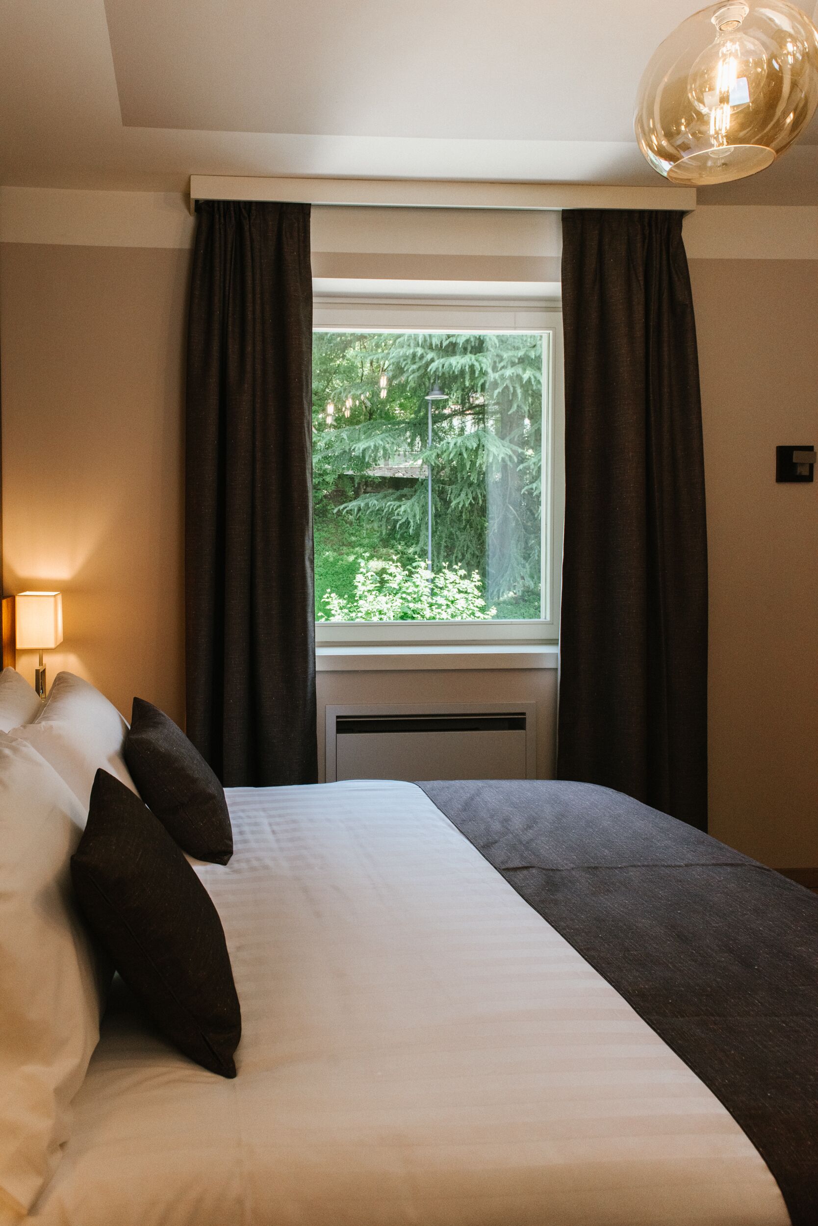A hotel room with a bed, a window with curtains, and a lamp.