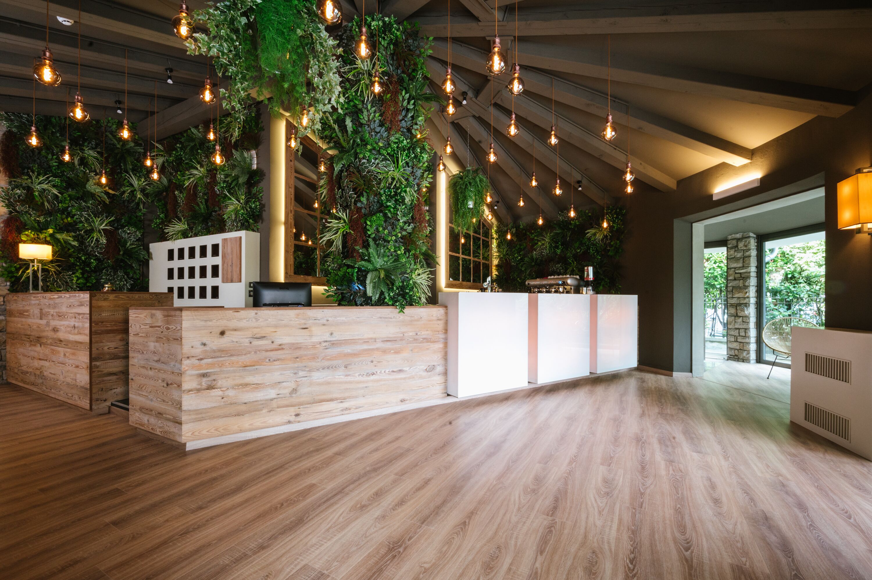 A reception area with a wooden reception desk, hanging pendant lights, and lush vertical greenery.