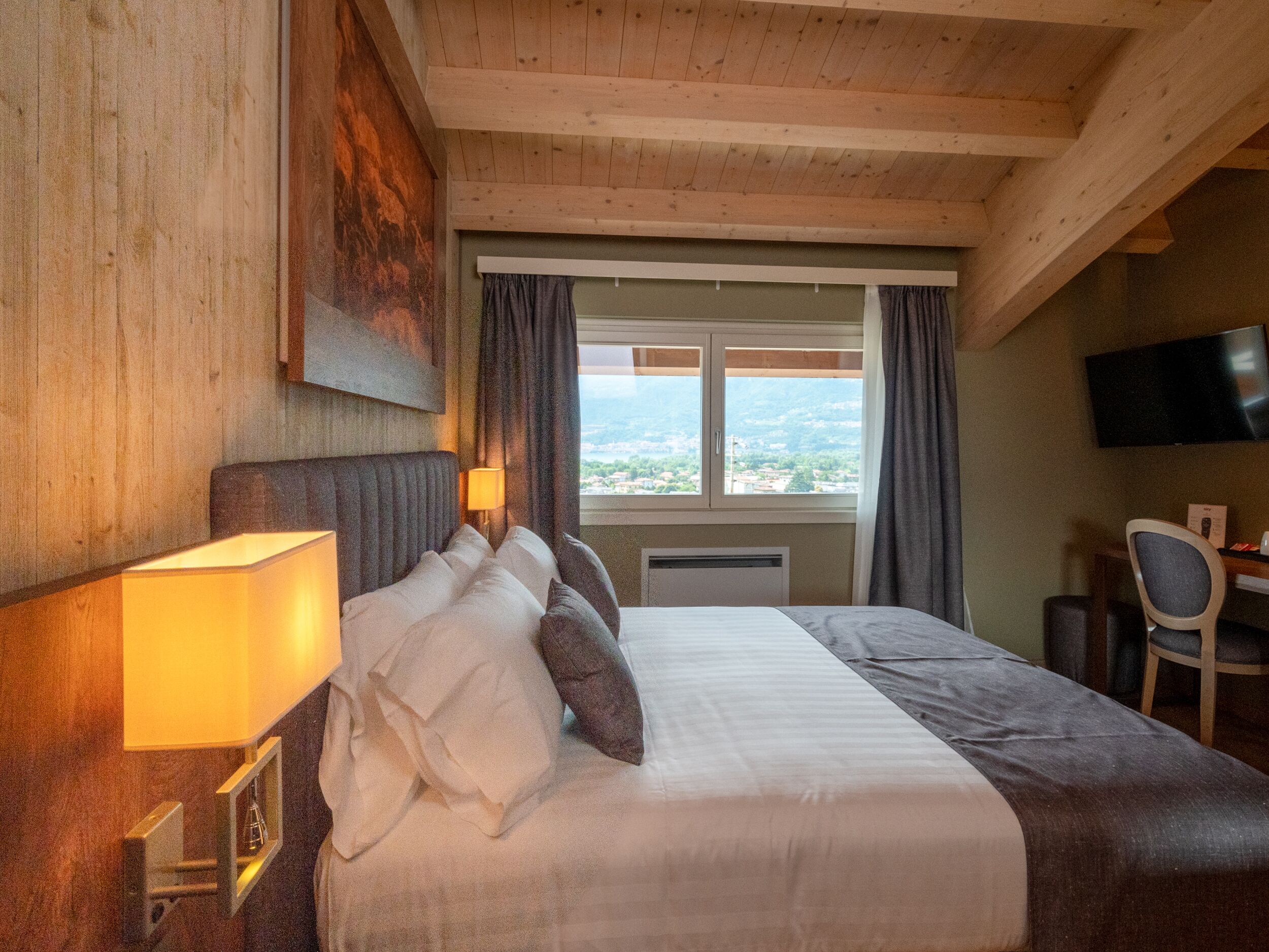 A hotel room with a large bed, a desk with a chair, a television, and a window with curtains.