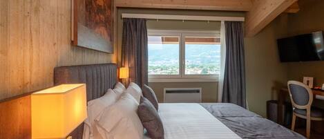 A hotel room with a large bed, a desk with a chair, a television, and a window with curtains.