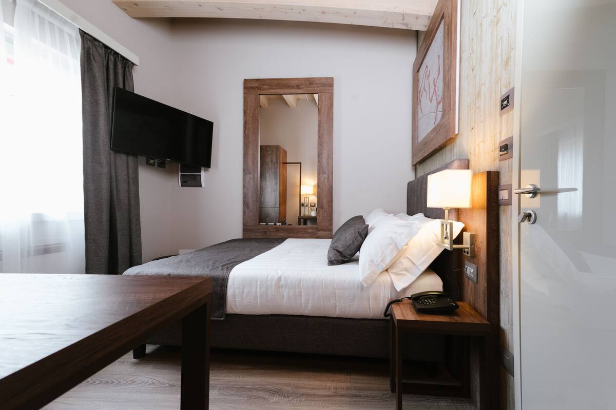 A hotel room with a bed, bedside table, lamp, and a flat-screen TV mounted on the wall.