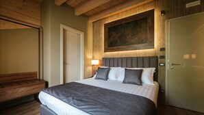 A bedroom with a large bed, a wooden bench, a door, and a wall-mounted artwork. - Lake Hotel La Pieve (Pisogne)