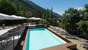 A swimming pool with lounge chairs and umbrellas, surrounded by trees and a mountain backdrop. - Lake Hotel La Pieve (Pisogne)