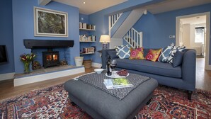 A living room with a blue wall, a fireplace, a sofa with colorful cushions, a patterned rug, and a bookshelf. - The Carriage House - sleeps 4 guests  in 2 bedrooms (Leyburn)