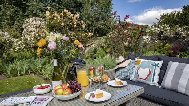 A garden setting with a table set for breakfast, including fruits, a bottle of wine, and glasses. - The Carriage House - sleeps 4 guests  in 2 bedrooms (Leyburn)
