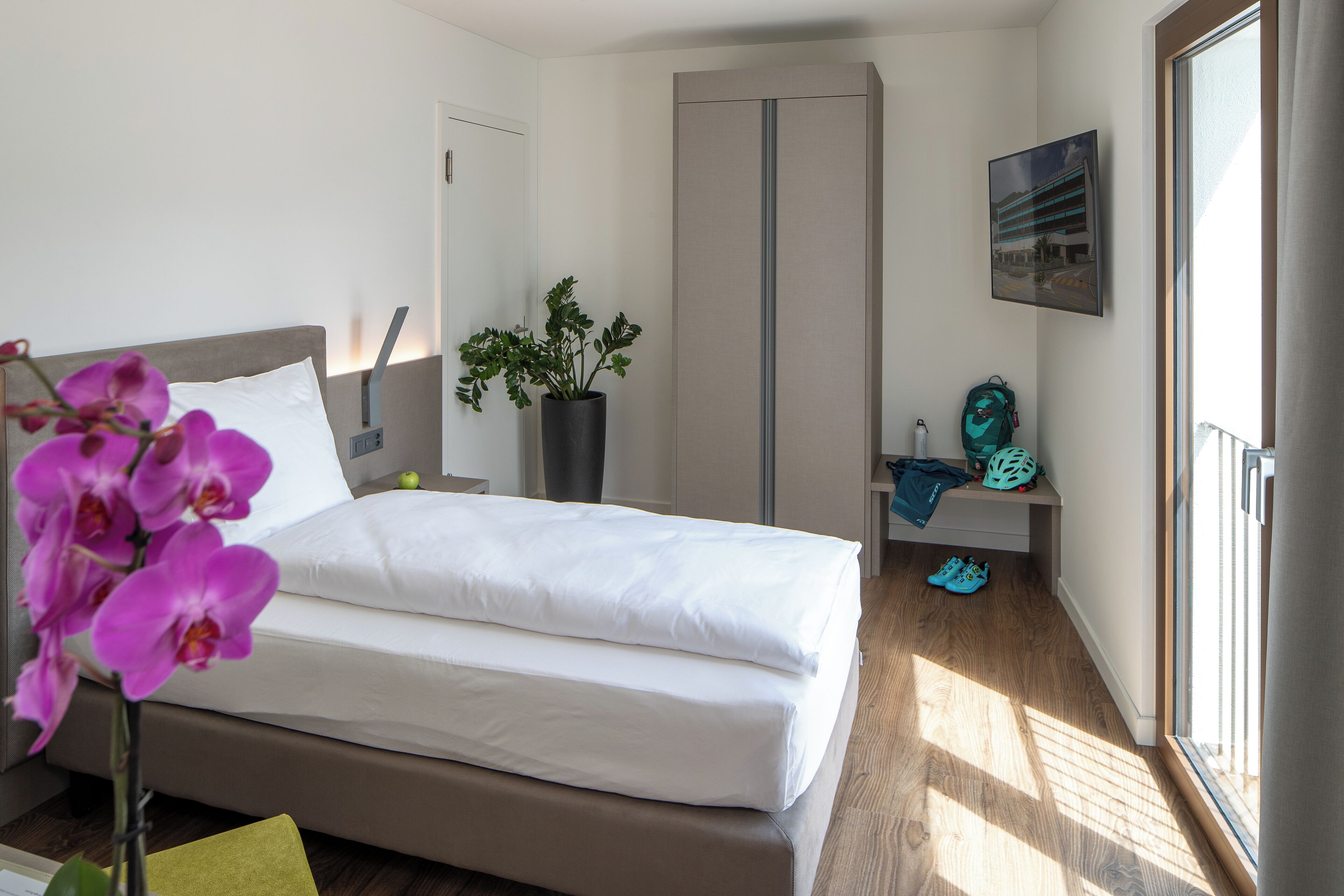 A bedroom with a bed, a potted plant, a backpack, and a pair of shoes on a bench.