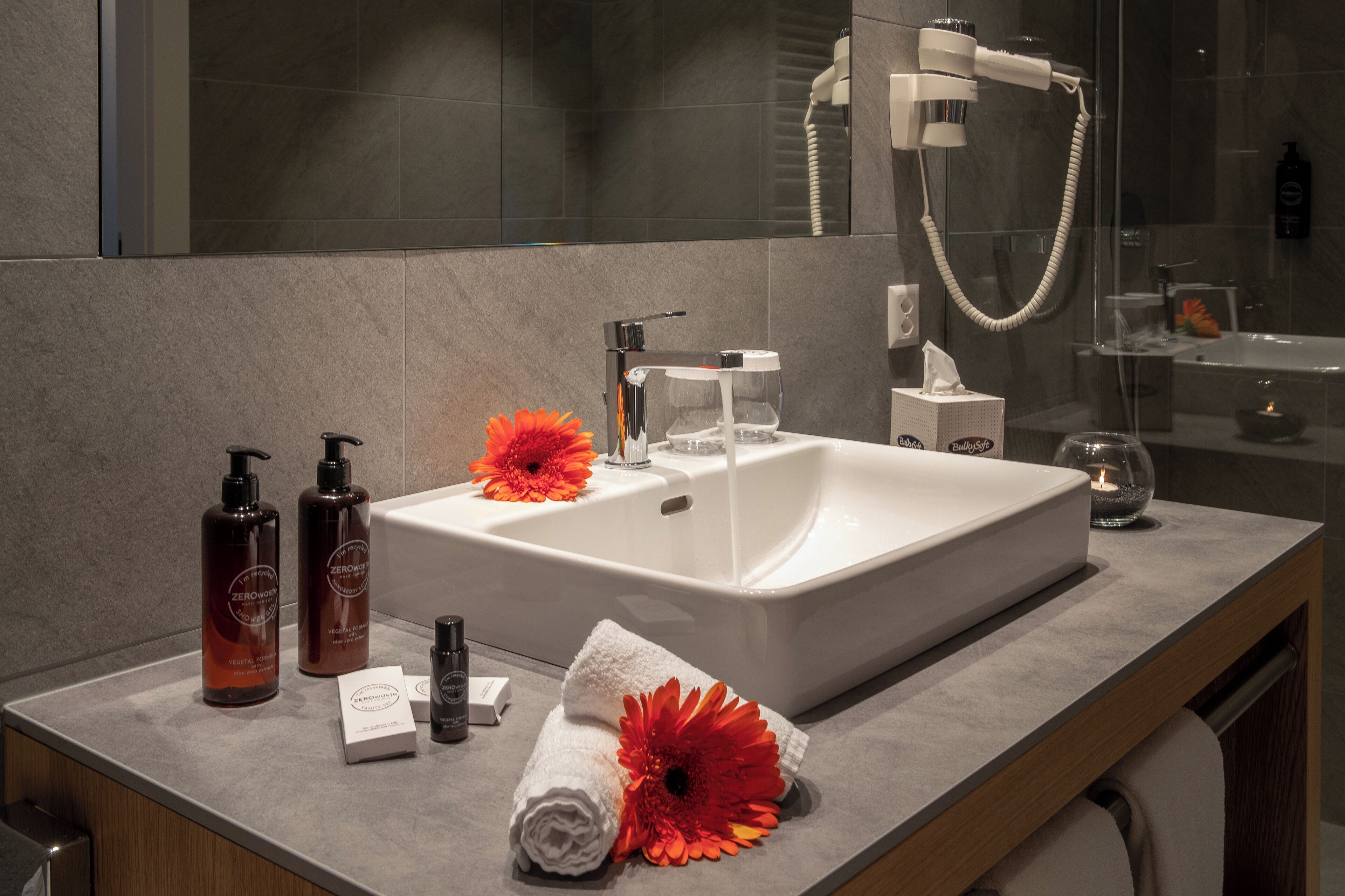 A modern bathroom with a large white sink, a handheld showerhead, and a glass-enclosed shower.