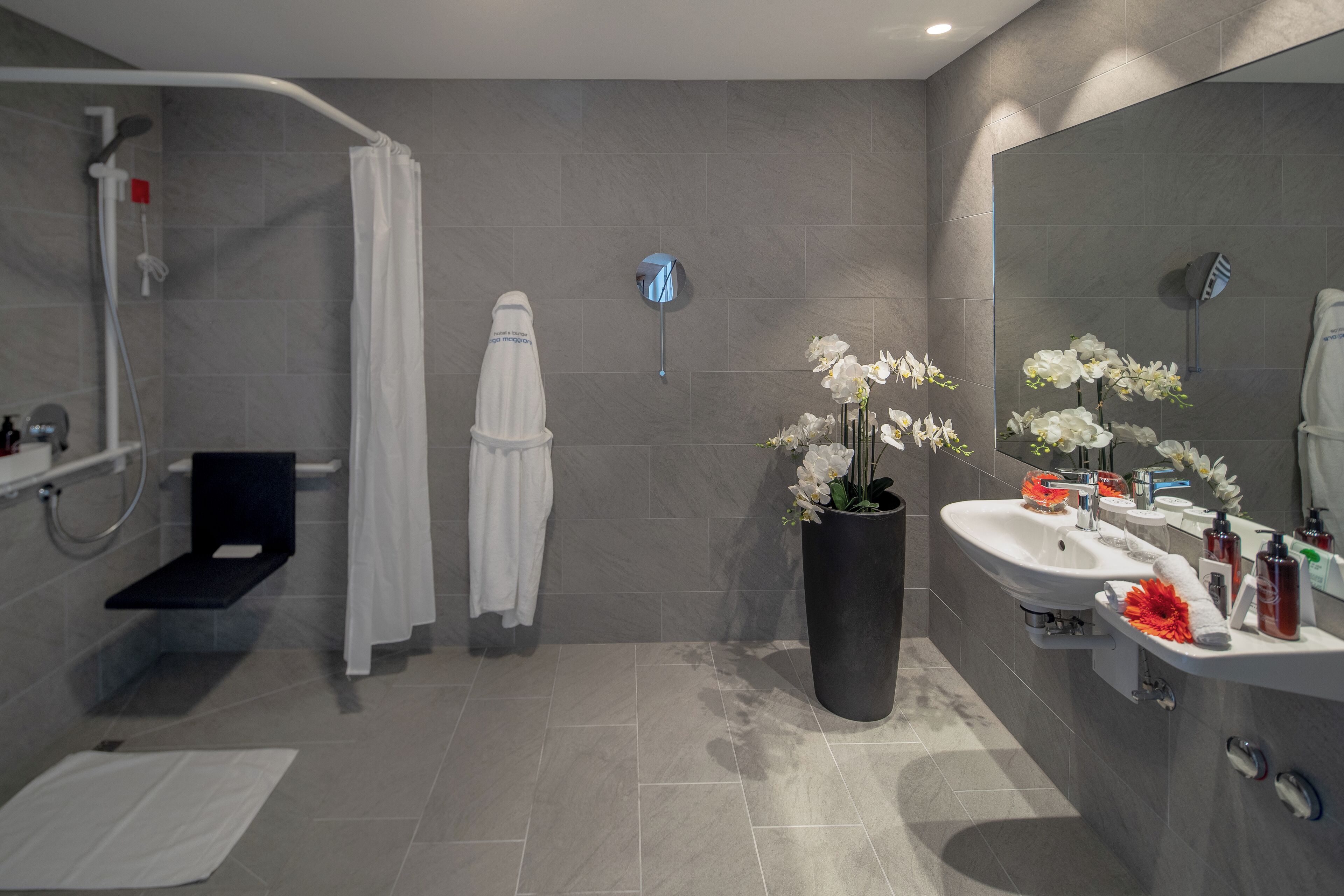 A modern bathroom with a shower, two sinks, a large mirror, and a potted orchid.