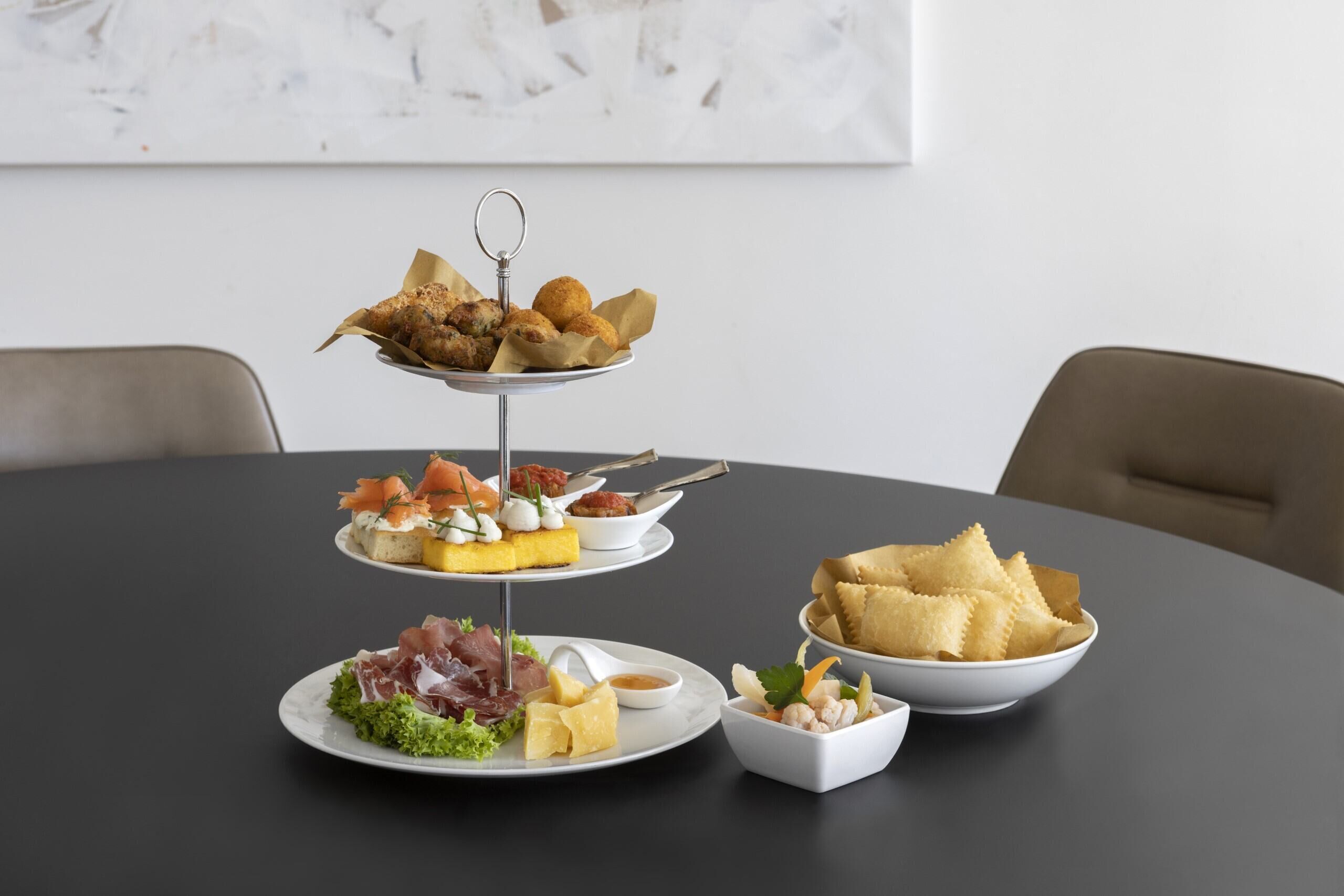 Un soporte de tres niveles para postres con diversos pasteles y un bol de galletas sobre una mesa redonda.