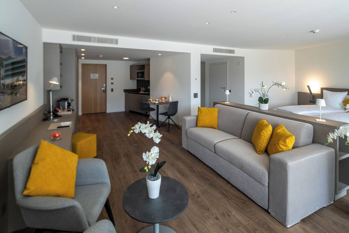 A modern living room with a grey sofa, yellow cushions, a grey armchair, and a round coffee table with a potted orchid.