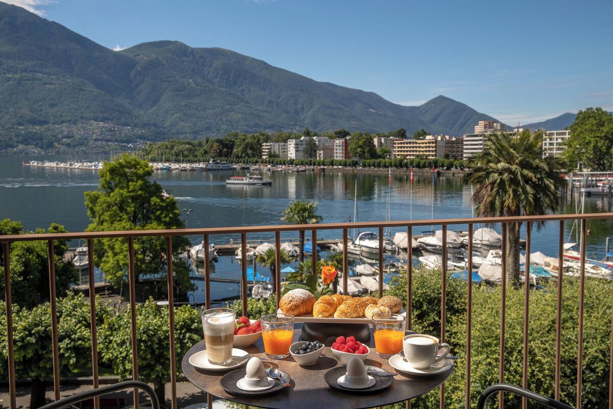 A table with breakfast items and a view of a marina and mountains.