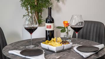 A round dining table with a bottle of Roncai wine, two glasses of red wine, a flower, and a bowl of chips.