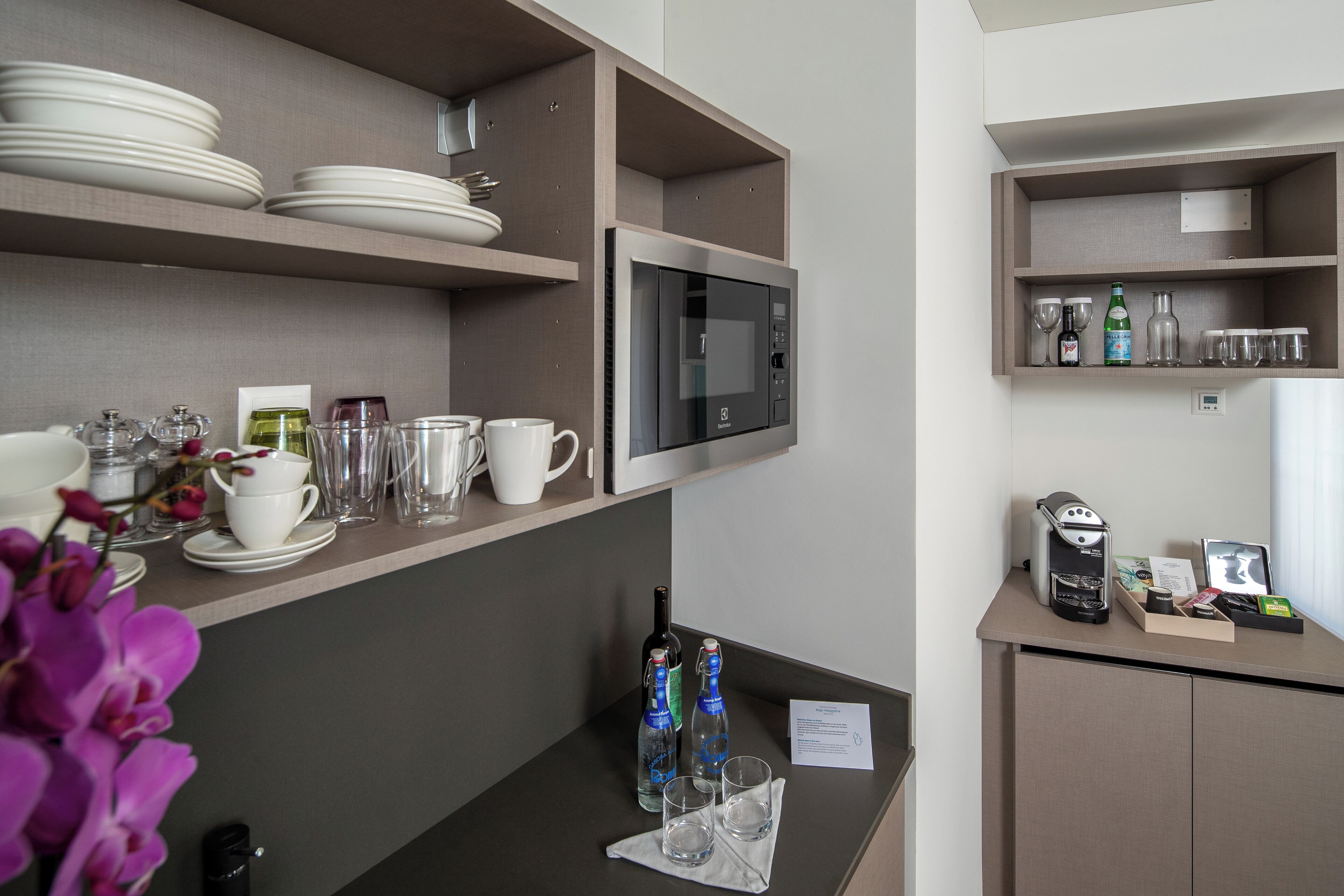 A hotel room with a kitchenette, a microwave, a coffee maker, and a small bar area with glasses and bottles.