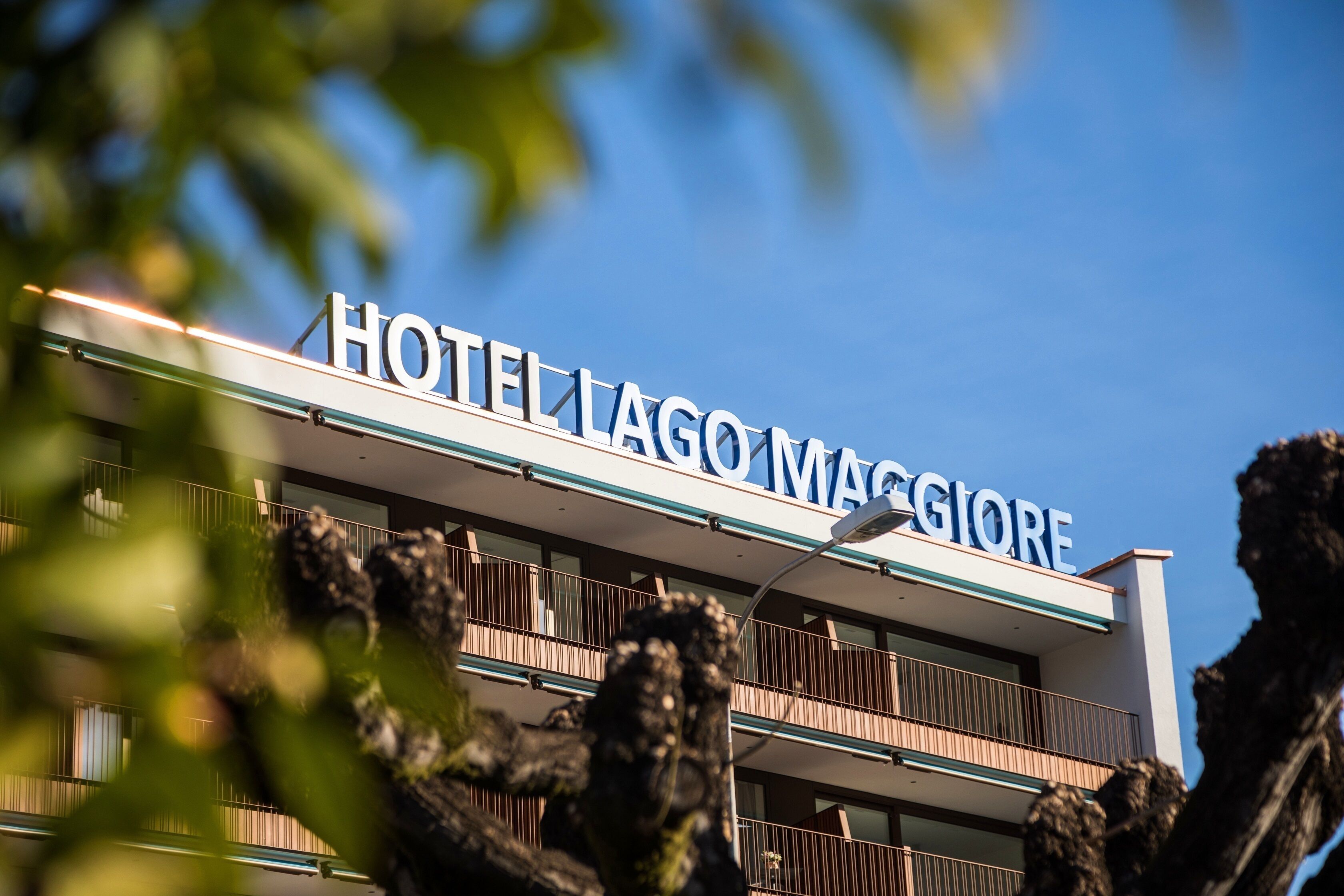 Hotel con un letrero que dice "HOTEL LAGO MAGGIORE" contra un cielo azul despejado.