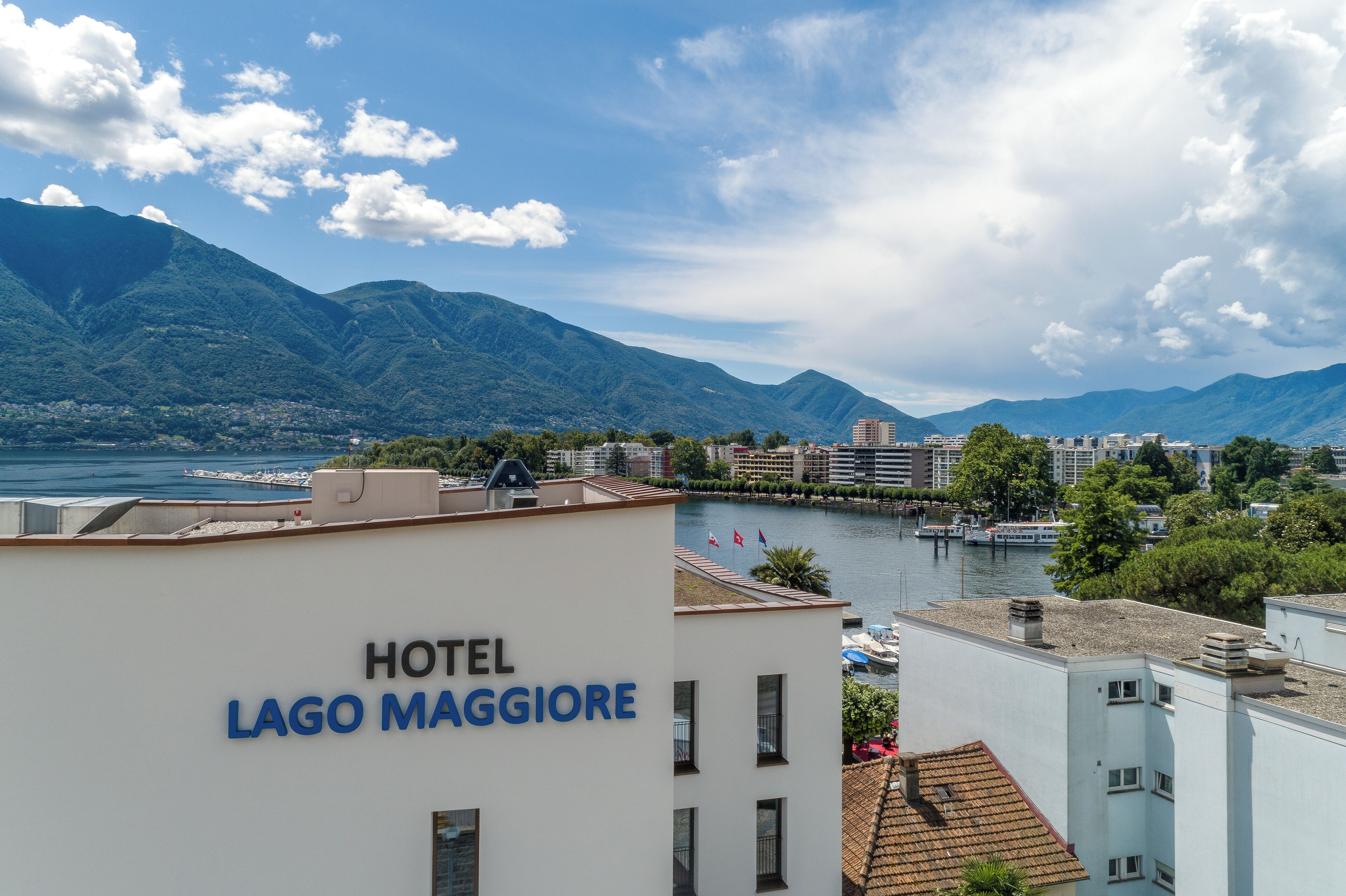 Un hôtel appelé «HOTEL LAGO MAGGIORE» offrant une vue sur les montagnes et un plan d’eau.