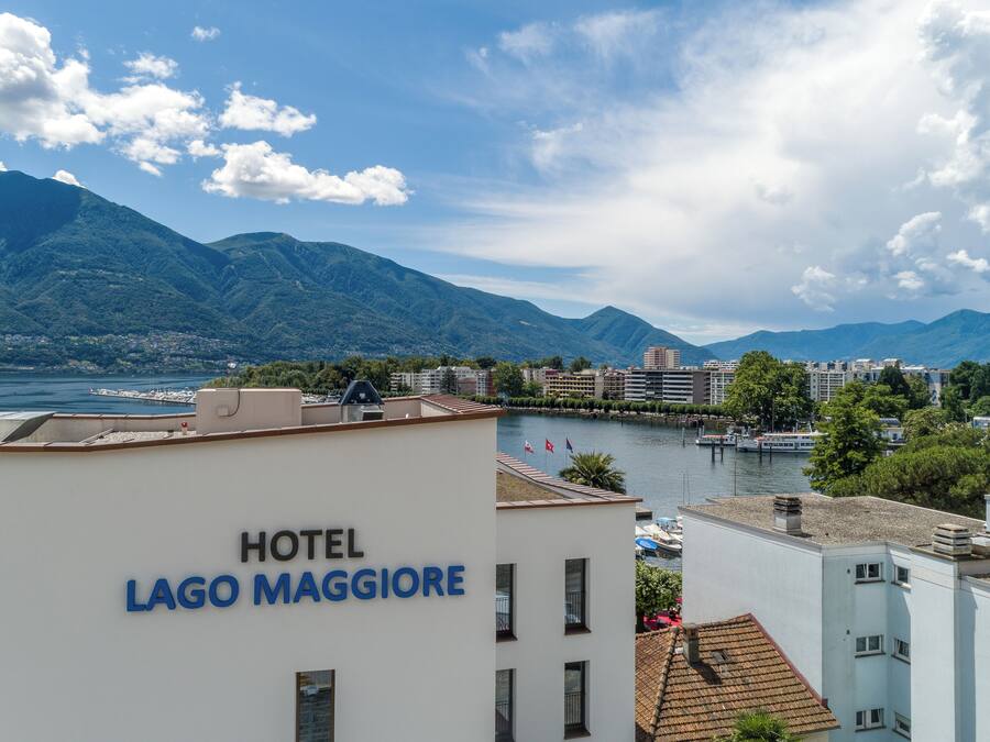 A hotel named "HOTEL LAGO MAGGIORE" with a view of mountains and a body of water.