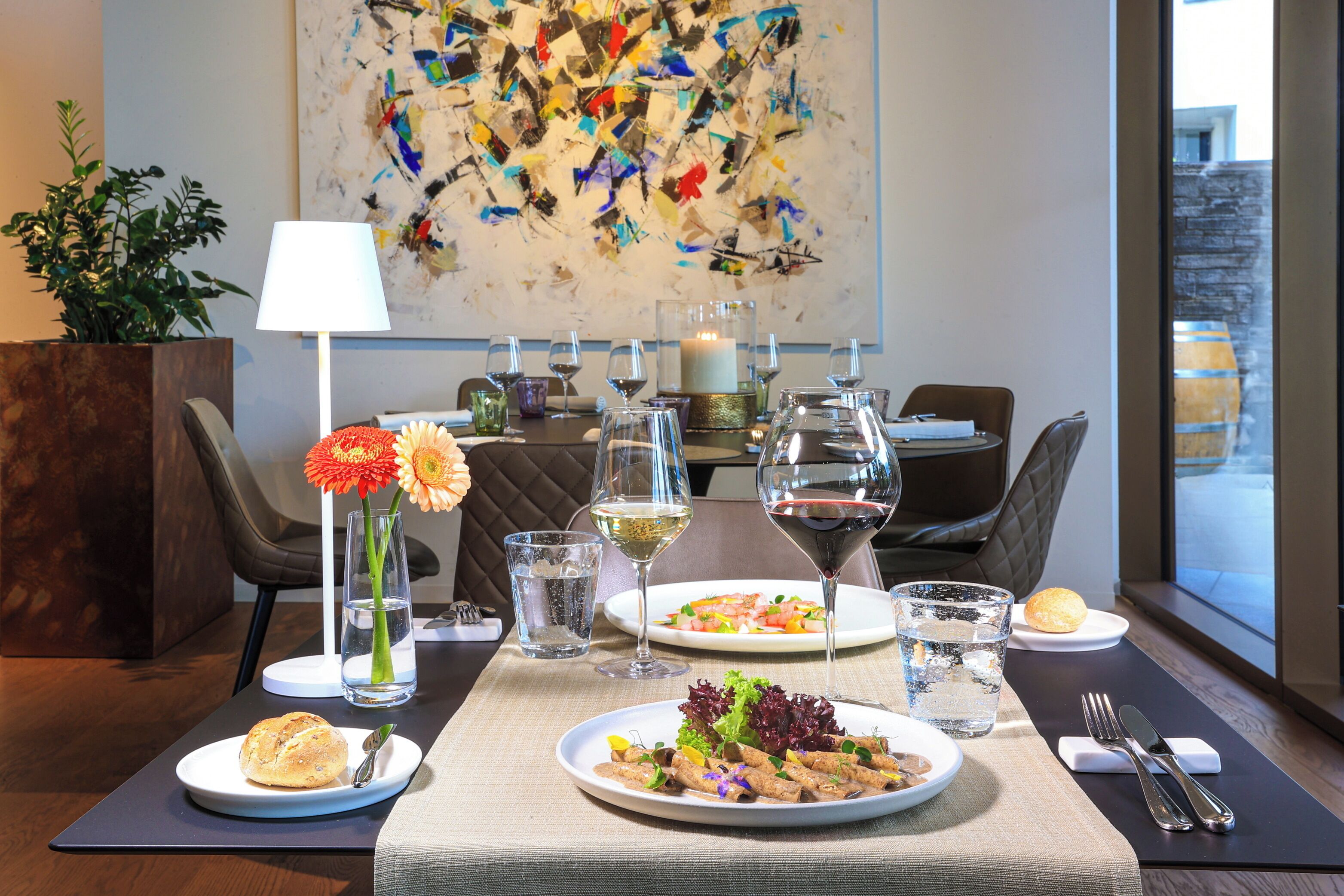A dining table set with plates of food, glasses of wine, and a vase of flowers.