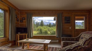 A cozy cabin interior with a large window offering a mountain view, a television, and a rustic wooden table. - Mica Mountain Lodge & Mica cabin at Mt Robson Park, near Jasper National Park (Tête Jaune Cache)