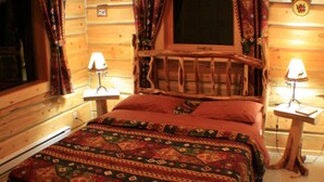 A log cabin bedroom with a wooden bed, patterned bedding, and two bedside lamps. - Mica Mountain Lodge & Mica cabin at Mt Robson Park, near Jasper National Park (Tête Jaune Cache)
