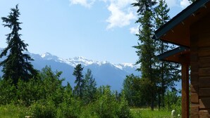 A wooden cabin with a deck overlooking a grassy area and a mountain range. - Mica Mountain Lodge & Mica cabin at Mt Robson Park, near Jasper National Park (Tête Jaune Cache)