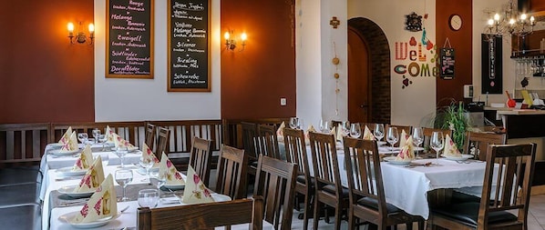 Un restaurant avec plusieurs tables dressées pour le service, un menu affiché au mur et une pancarte indiquant « Bienvenue ».